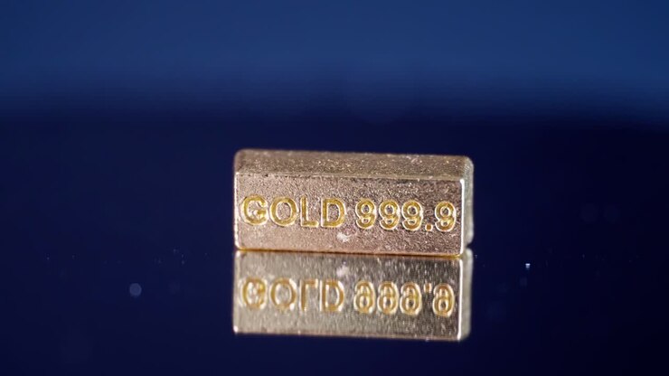 Small gold bar stamped 9999 rotates on a reflective disc in dark surroundings, symbolizing wealth and finance