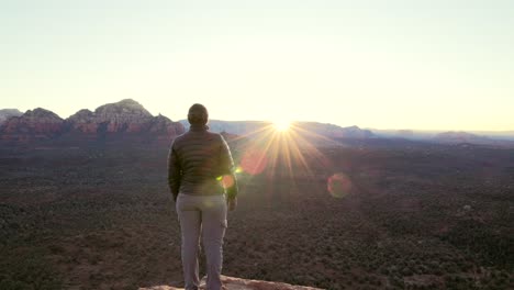 excursionista se encuentra en un acantilado al amanecer observa la cresta del sol sobre las cimas de las montañas en sedona