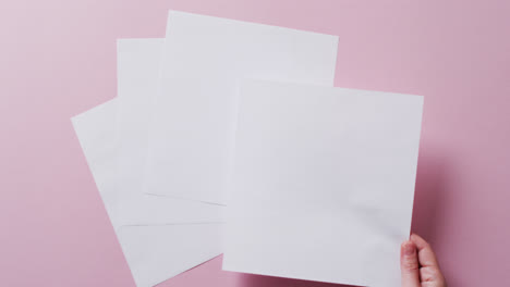 Hand-holding-piece-of-paper-over-pieces-of-paper-with-copy-space-on-pink-background-in-slow-motion