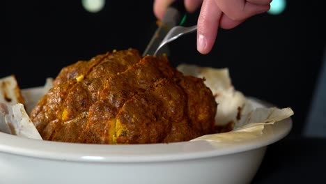 man chef slicing a whole roasted and spiced cauliflower