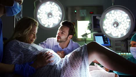 doctor examining pregnant woman during delivery while man holding her hand in operating room