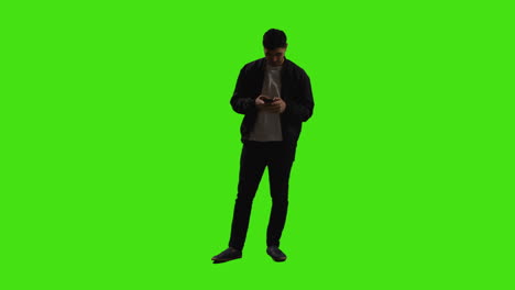 joven hablando en el teléfono móvil de pie contra la pantalla verde con poca iluminación clave