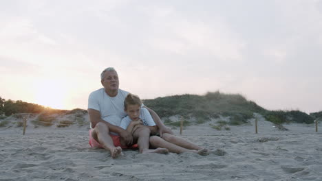 el abuelo y el nieto están sentados en las dunas