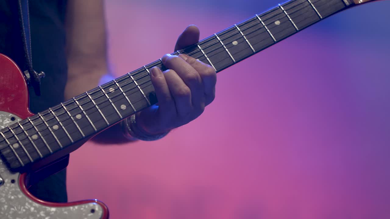 Konser sahnesinde elektro gitar çalan rock grubundaki adam, yakın çekim el görüntüsü.