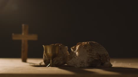 concepto religioso filmado con cáliz pan roto cruz y vino sobre mesa de madera contra fondo negro 2