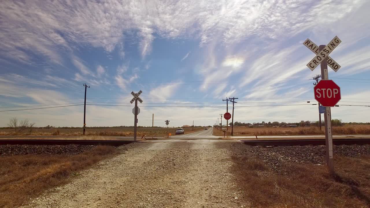 coche acercándose a un cruce de ferrocarril en medio de la nada, largo camino con amplios campos abiertos y cielos azules y soleados