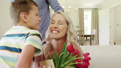 padre con sus hijos dando un regalo sorpresa a la esposa en la sala de estar