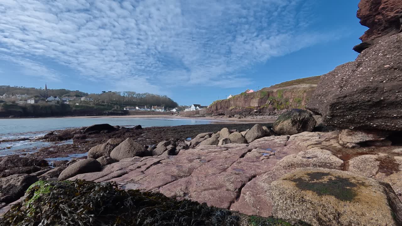 Vista da Aldeia de Dunmore East, Waterford, Irlanda, através da praia na maré baixa, com rochas vermelhas e praia tranquila no início da primavera, antes da estação turística.