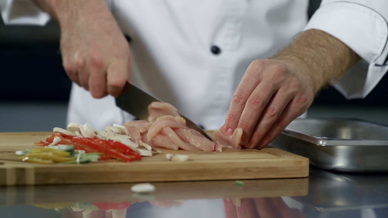 Mani dello chef che tagliano la carne in cucina. Primo piano delle mani dello chef che tagliano il filetto di pollo.