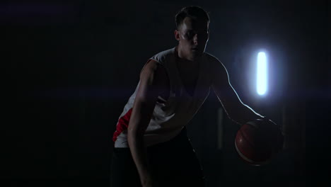 a basketball player dribbles down the court out of the shadows