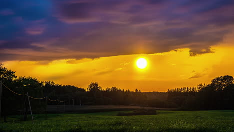 Amanecer-Dorado-Detrás-De-Cúmulos-Púrpuras-Sobre-Un-Prado-Verde