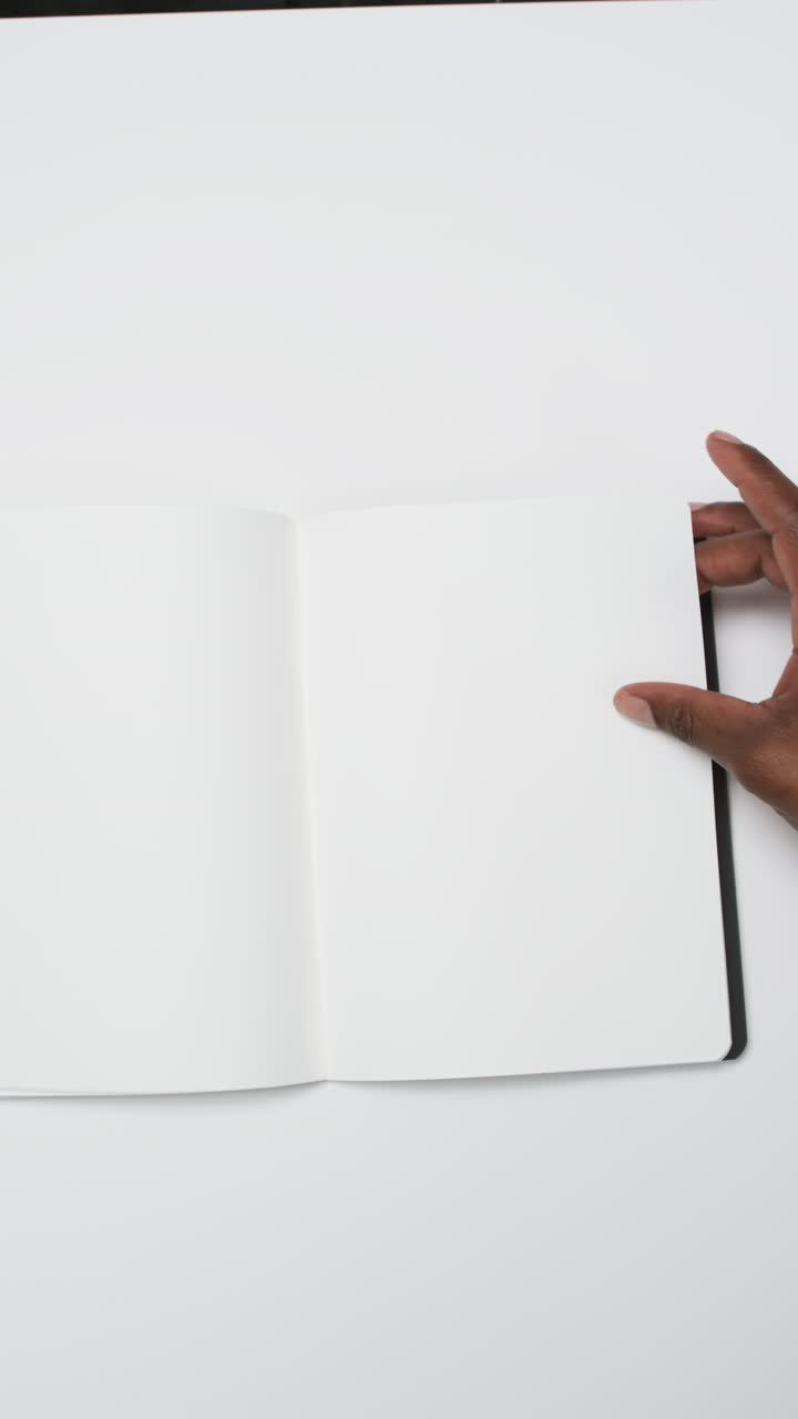 Vertical video of hand of african american man with book with white blank pages on white background