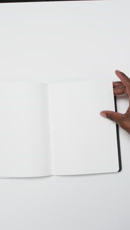 vertical video of hand of african american man with book with white blank pages on white background
