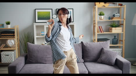 woman dancing and singing in living room with headphones and remote