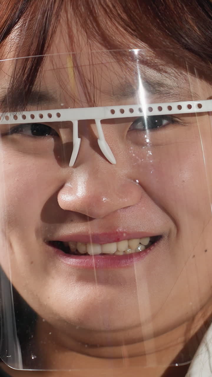 보호 얼굴 방패를 착용하는 학생은 눈을 이고, 기계 작업장에서 따뜻한 미소로 웃고, 배경에는 산업 도구, 밝은 조명 및 기계가 있습니다.