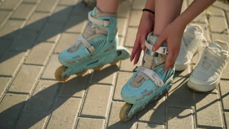 partial view of individual adjusting roller skate strap on left leg with black wristband under warm sunlight, white sneakers lying nearby on pavement, with greenery softly blurred in background