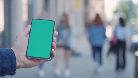 4k close-up man's hand holding smartphone with green screen on street in city