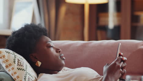 Afroamerikanische-Frau,-Die-Auf-Der-Couch-Liegt-Und-Ihr-Smartphone-Benutzt