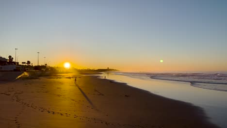 Vista-Estática-De-Gente-En-La-Playa-Caminando-Bajo-La-Luz-Naranja-Del-Atardecer