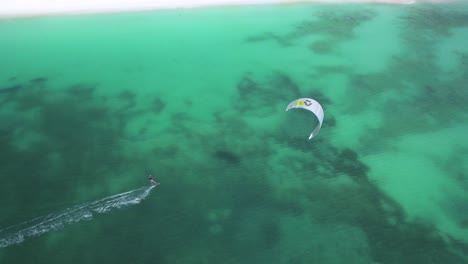 A-kitesurfer-gliding-over-turquoise-waters-near-crasky-beach,-aerial-view