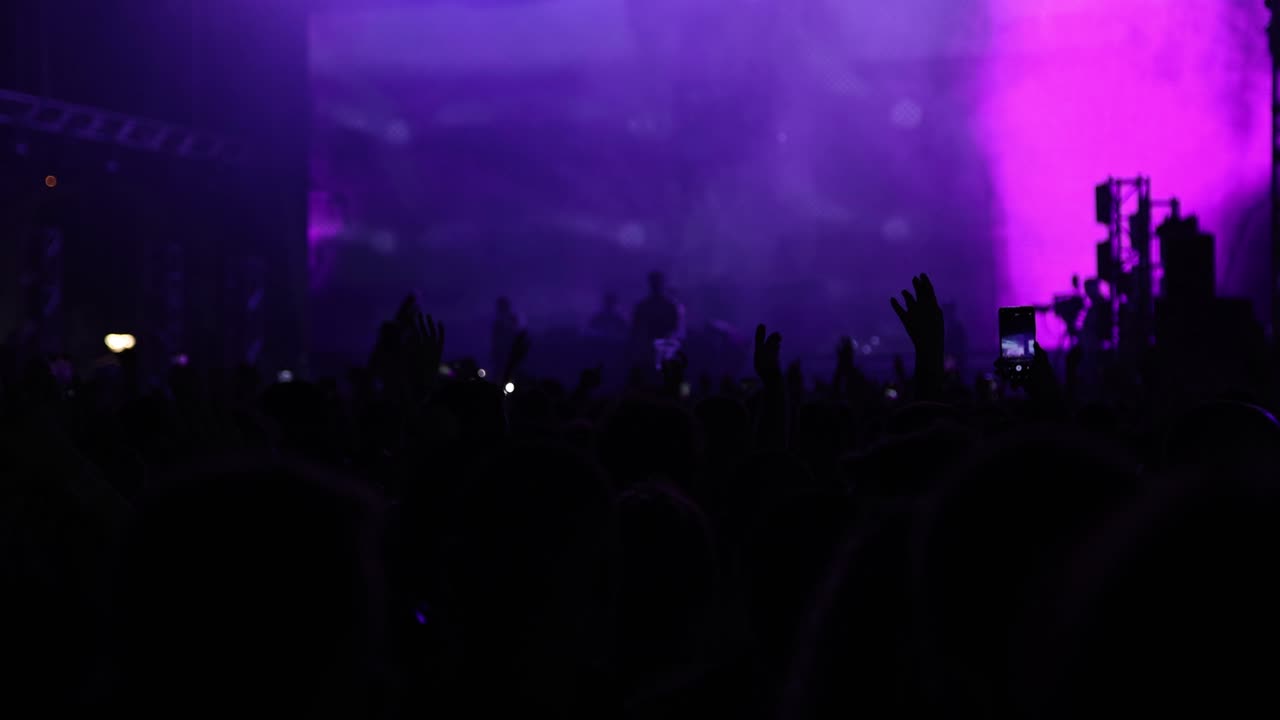 Gruppo musicale che canta sul palco in controluce, effetti di luci al neon da concerto davanti alle silhouette dei fan