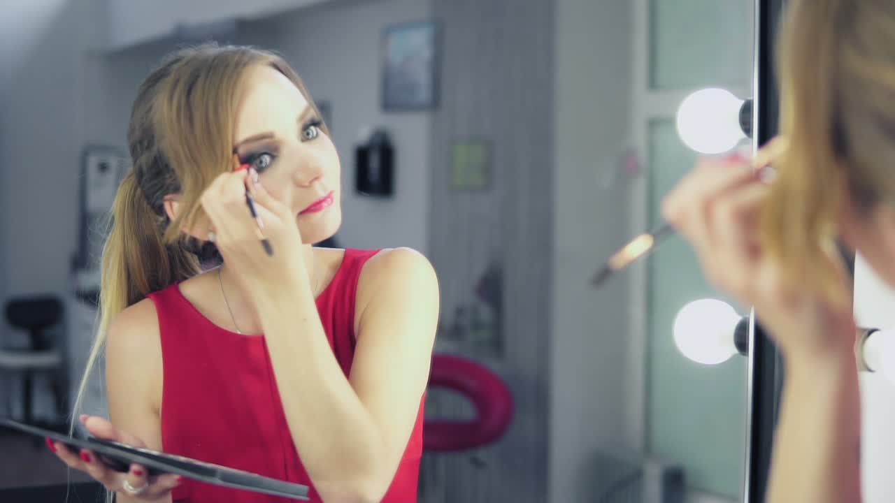 reflejo en el espejo de una mujer joven en vestido rojo pintando sus cejas. disparo en cámara lenta