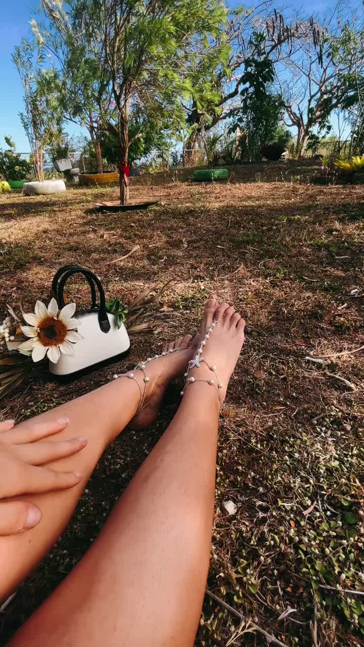 mujer relajándose en un jardín con sandalias y bolso