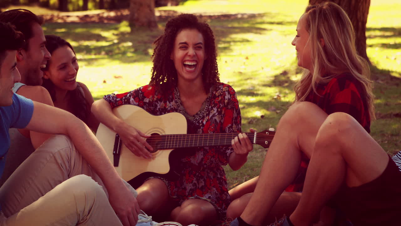 Happy friends in the park having picnic and playing guitar
