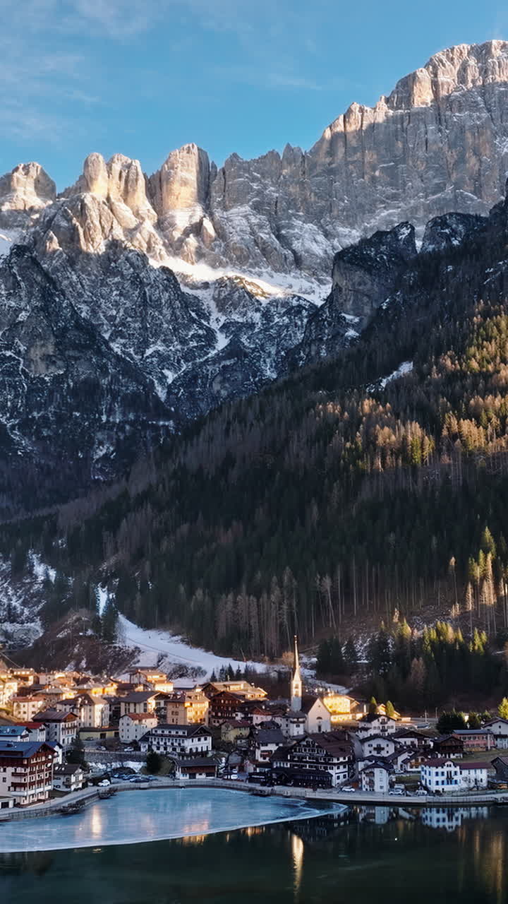 Aerial drone view of the Alleghe village with Lake Alleghe, in the province of Belluno, Dolomites, Italy. Vertical
