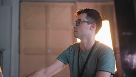 person focused on adjusting video equipment in tv studio, working with control panel and monitor displaying broadcast setup. bright light in background, studio lighting and cables visible