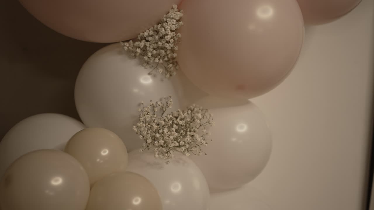 decorative arrangement featuring white and light pink balloons grouped together, complemented by small clusters of delicate white flowers, creating an elegant and festive atmosphere