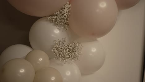 decorative arrangement featuring white and light pink balloons grouped together, complemented by small clusters of delicate white flowers, creating an elegant and festive atmosphere