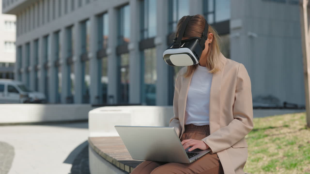 Молодая женщина в VR-гарнитуре печатает на ноутбуке на улице.