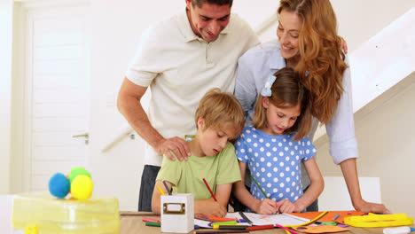 padres y hijos felices dibujando juntos en la mesa mirando a la cámara