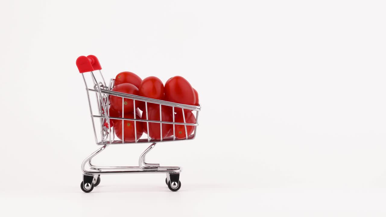 Sich bewegender Einkaufswagen gefüllt mit roten Kirschtomaten. Isoliert auf weißem Hintergrund. Nahaufnahme. Makro