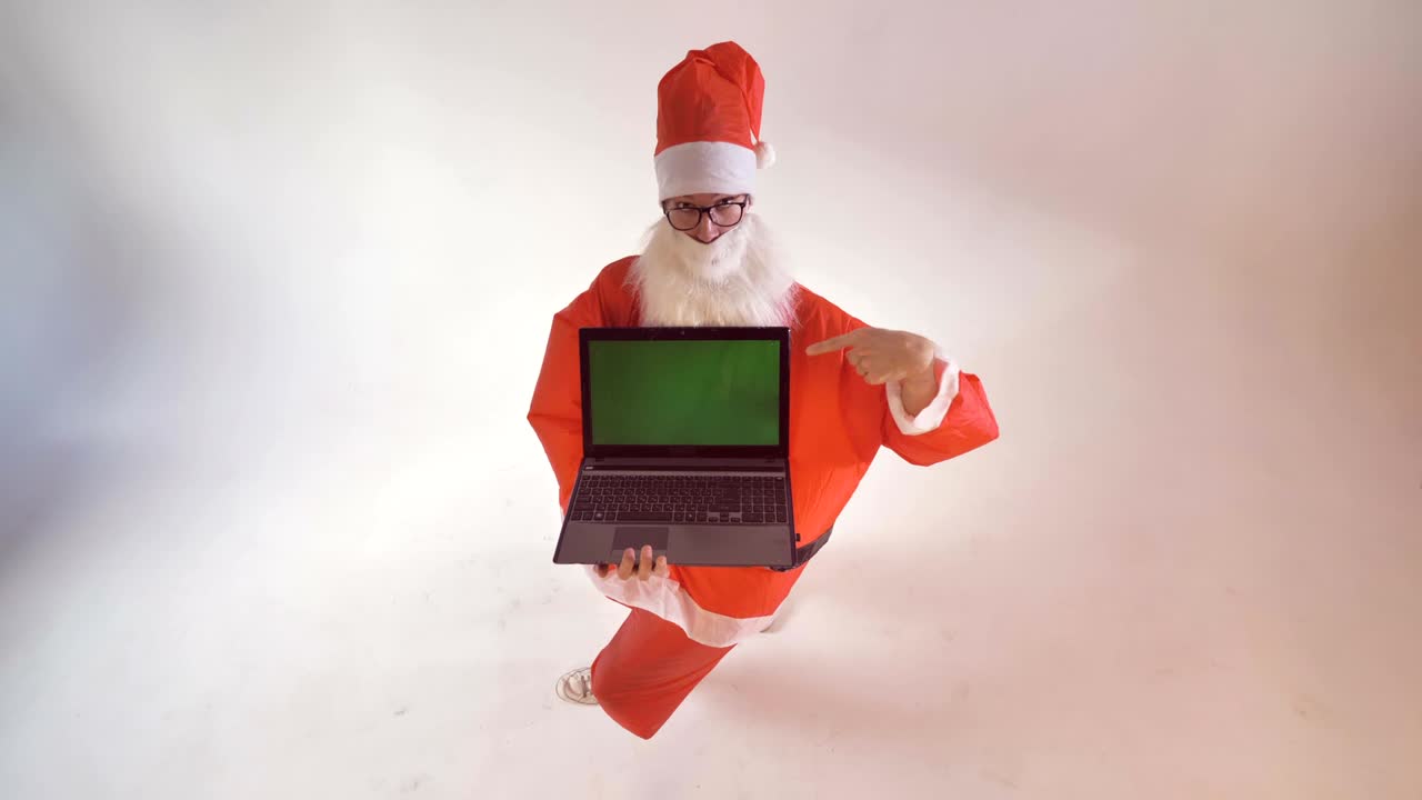 산타클로스는 돌아서서 초록색 배경의 새 노트북 화면을 보여줍니다.
