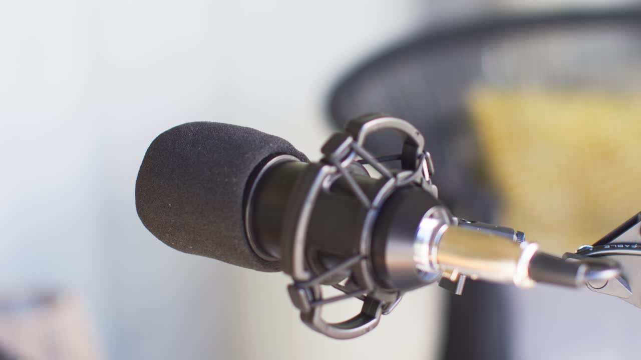 Camera is pulling focus and tightening framing, making foam cardioid mic appear sharper for podcast