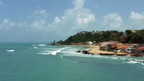 aerial drone wide landscape shot of the tropical famous baia formosa beach town in the state of rio grande do norte, brazil with fishing boats, coastal homes, small waves, and surfers