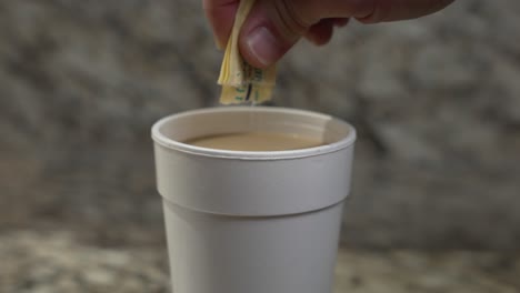 el azúcar se está vertiendo en una taza de estirofoam en un mostrador de mármol