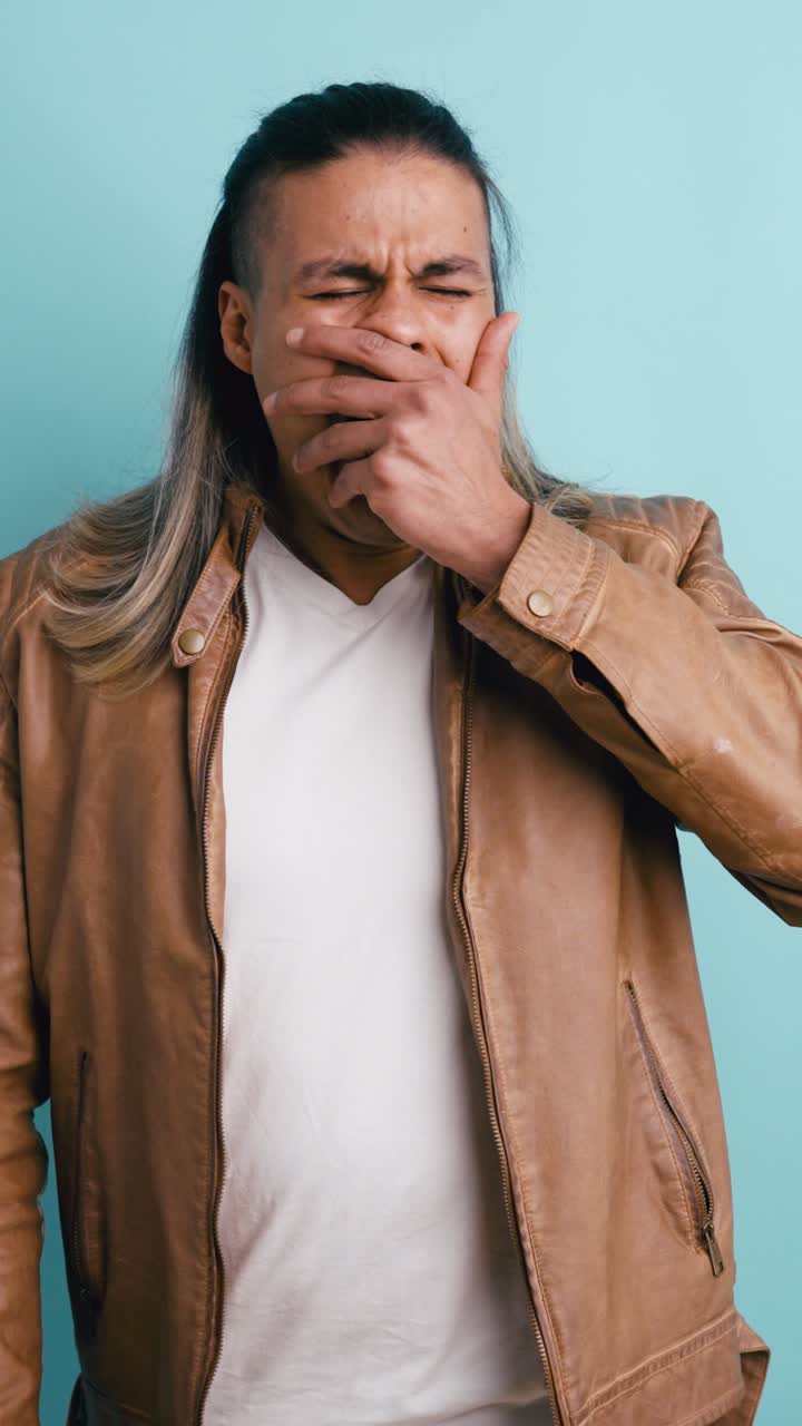 Giovane uomo che sbadiglia e si copre la bocca in studio.