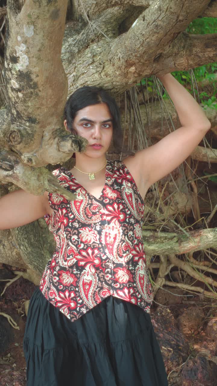 Woman posing by intricate tree in stylish attire, serene outdoor vibe
