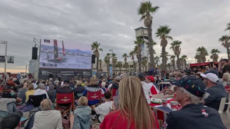 crowd outside watching the 37th america´s cup on a giant screen. sailboat on the screen