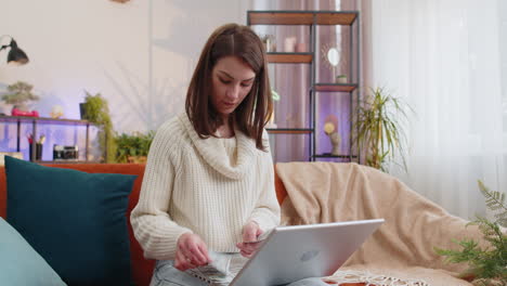 Una-Mujer-Feliz-Y-Sonriente-Contando-Dinero-En-Efectivo-Y-Usando-Una-Computadora-Portátil-Para-Calcular-Los-Ingresos-Domésticos-En-Casa