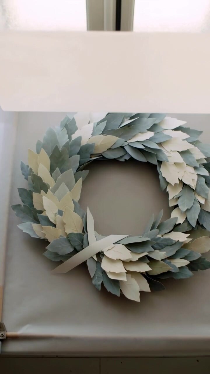 Vertical video: Lifting vellum roll after hand tug, revealing paper leaf wreath on mat for display