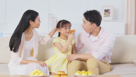 happy family of three sitting on the sofa enjoys a meal eating mooncakes together while celebrating the mid-autumn festival