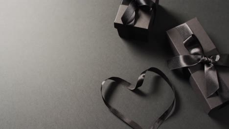 Two-black-gift-boxes-with-black-ribbons-and-ribbon-in-heart-shape,-on-dark-grey-with-copy-space