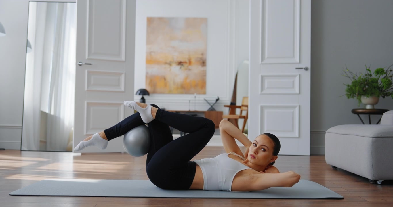 Giovane donna che esegue sollevamenti delle gambe Pilates con la palla a casa