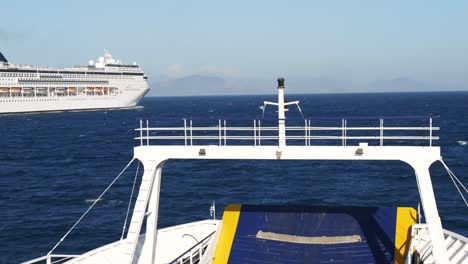 view of the bow of a ferry sailing through the blue waters of the ionian sea with a cruise ship in the background