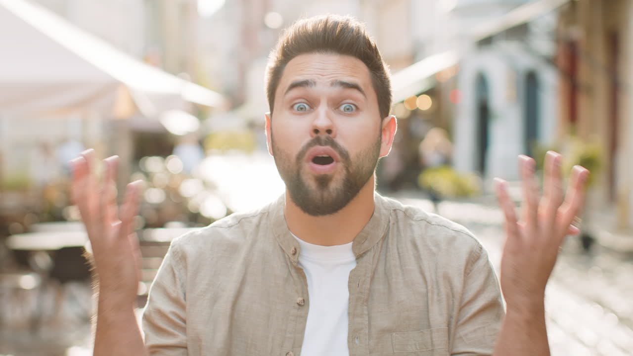 Young man looking surprised at camera shocked by sudden win good victory news wow in city street