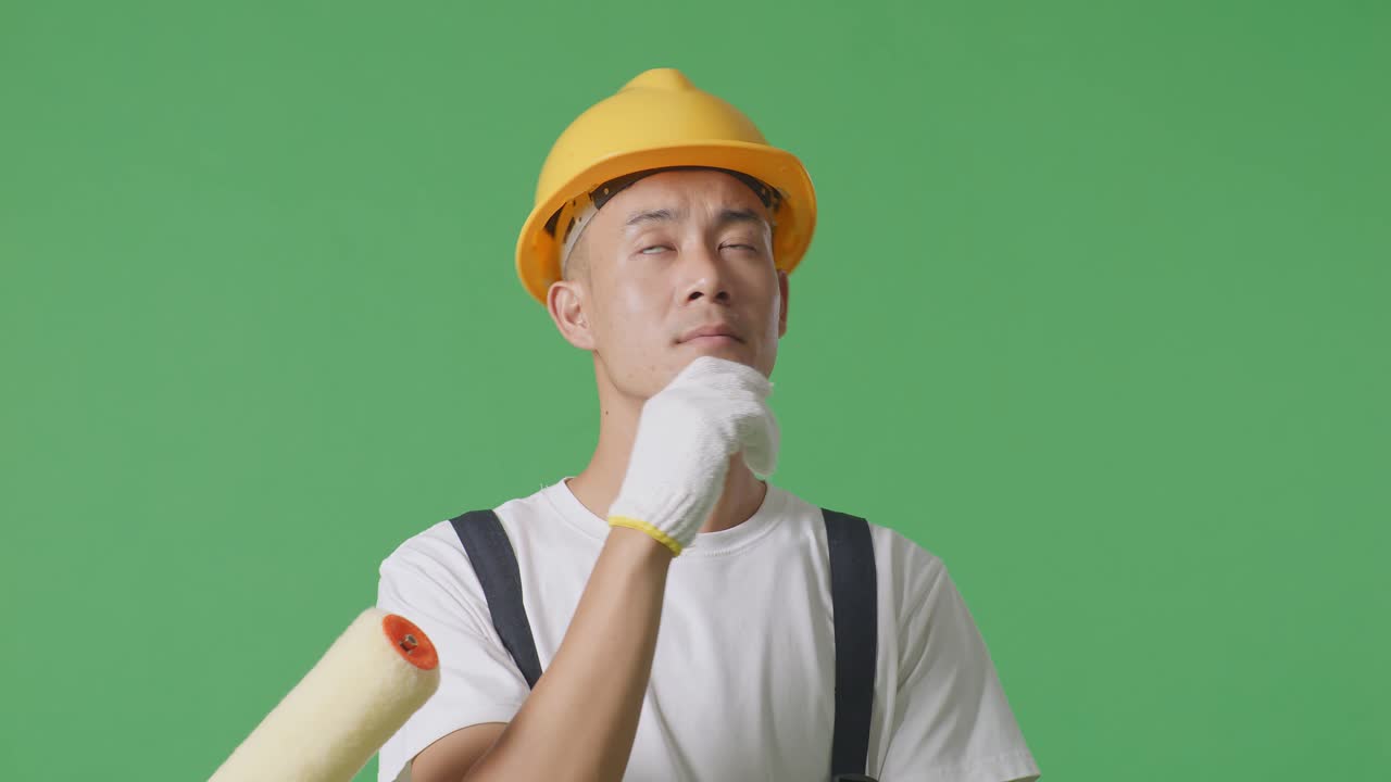 Close Up Of Asian Man Painter Wearing Safety Helmet Thinking And Looking Around Then Raising His Index Finger While Standing In The Green Screen Background Studio